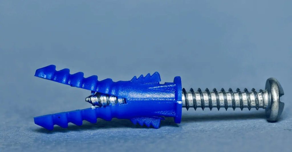 Blue plastic drywall anchor with metal screw on gray surface
