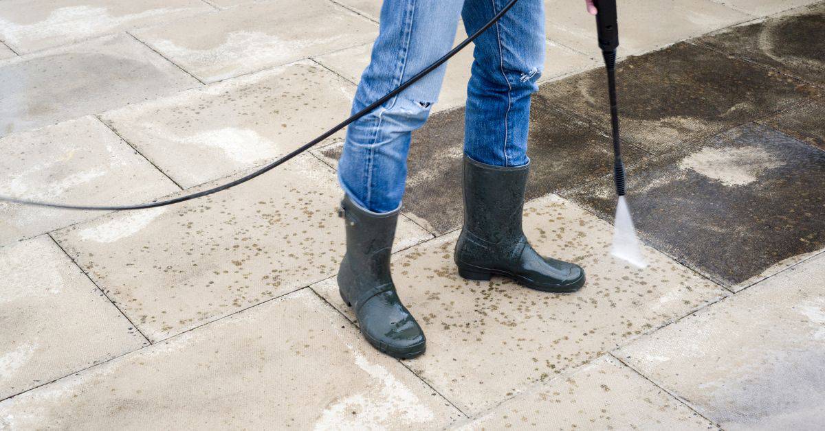Person wearing jeans and boots pressure washing stone pavers