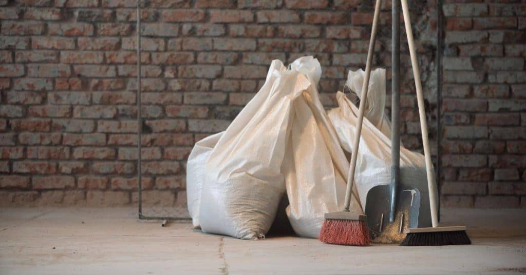 Brooms and shovel leaning against white sacks on floor