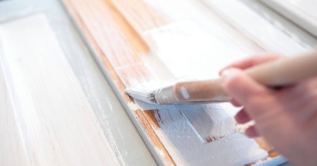 Close-up of hand painting wood door with white paintbrush