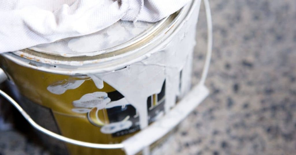 Close-up of paint can with white paint spilled on side