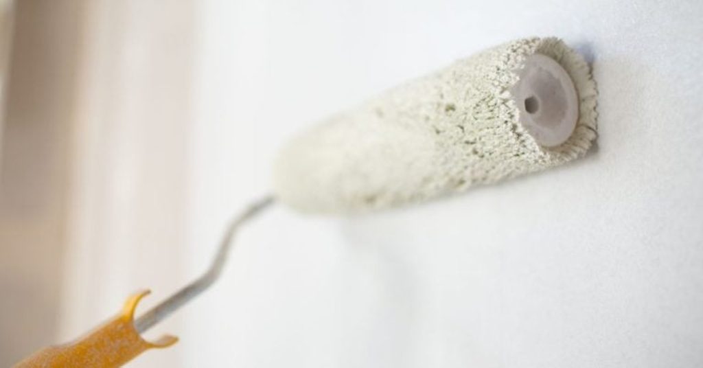 Close-up of paint roller applying light-colored paint on white wall