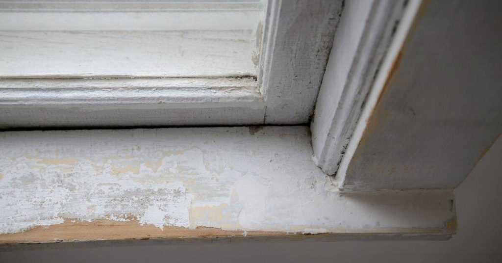 Close-up of peeling paint on white exterior wooden window trim