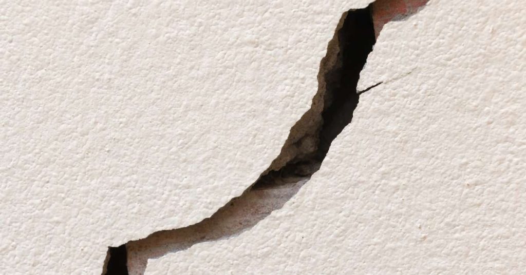Closeup of deep irregular crack in textured stucco wall