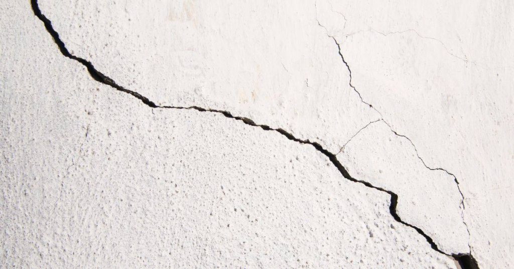 Closeup of large crack in white stucco wall surface