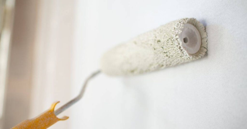 Closeup of paint roller applying white paint on wall