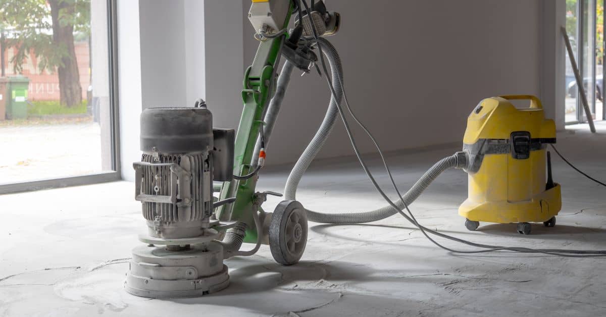 Concrete floor grinder connected to yellow vacuum cleaner indoors