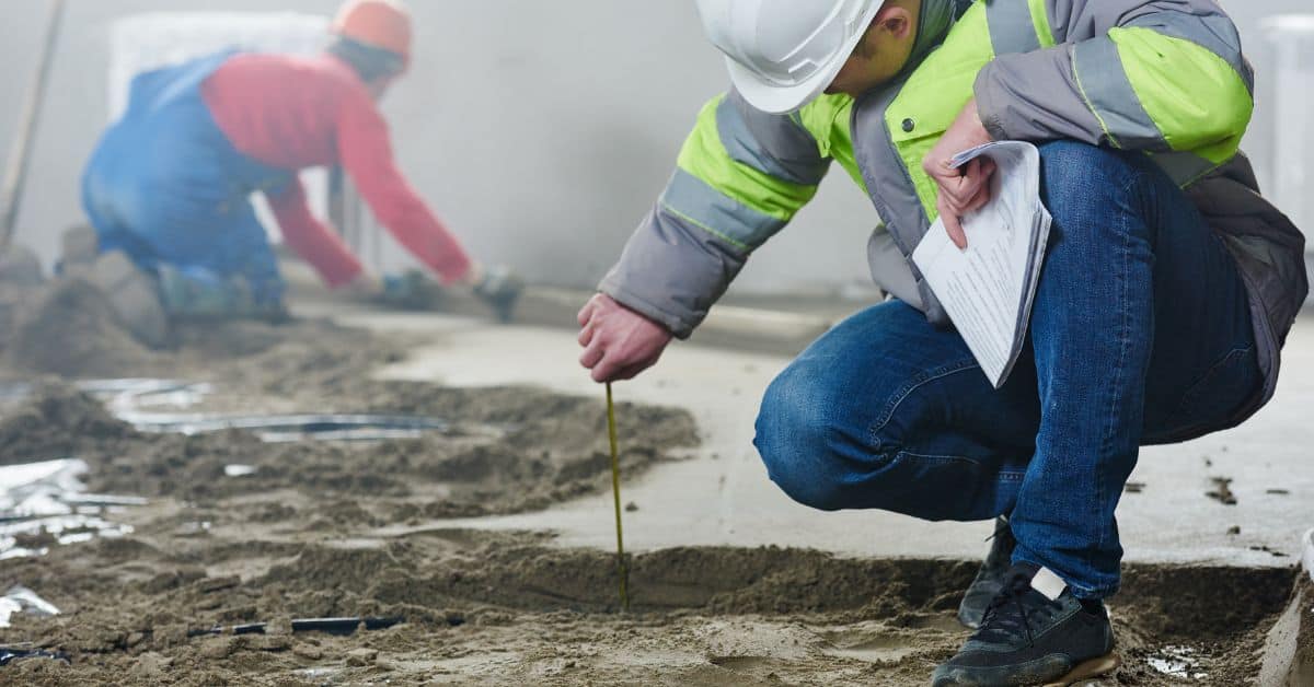 Worker measuring depth of wet concrete slab with tape measure