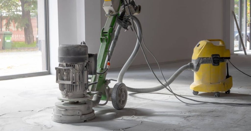 Concrete floor grinder connected to yellow vacuum cleaner indoors