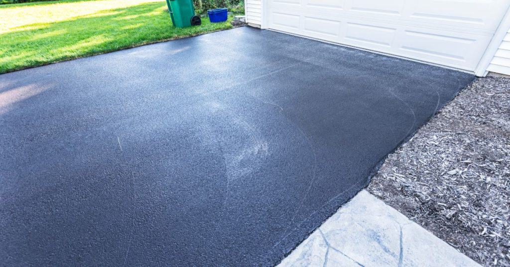 Freshly paved black asphalt driveway leading to white garage