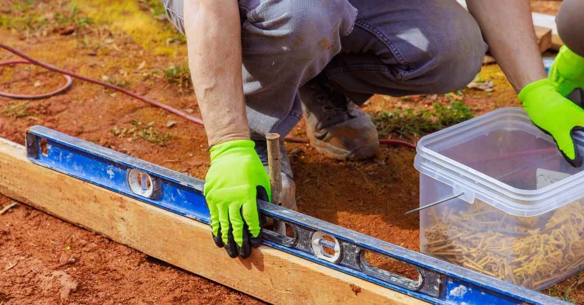 Worker using level tool on wooden form for concrete with screws nearby