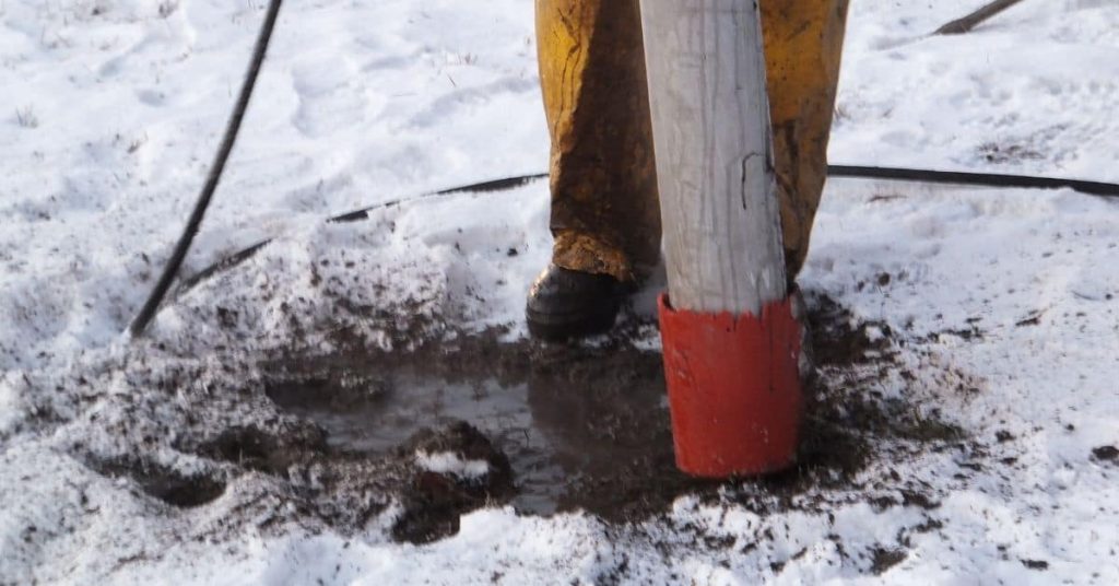 Concrete pouring hose in snowy ground with worker boots