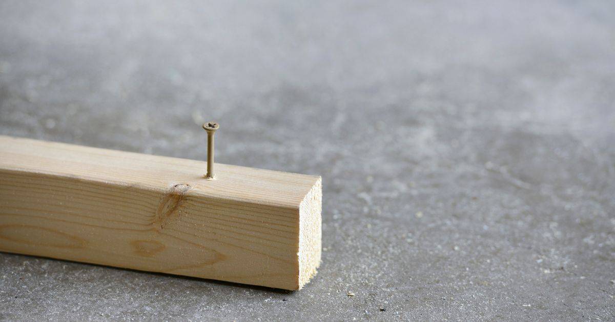 Wood block with nail partially driven into concrete surface