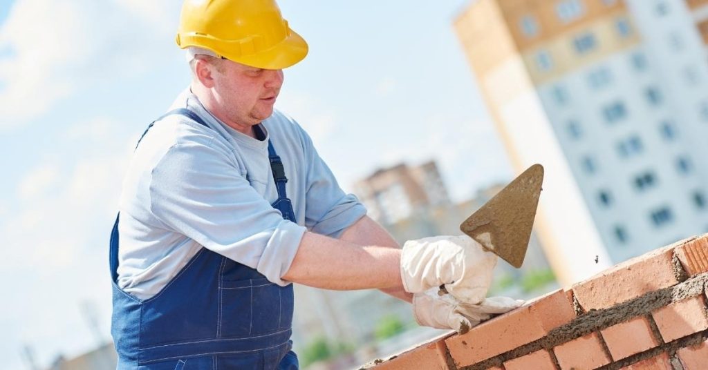 Construction worker laying mortar on brick wall outdoors