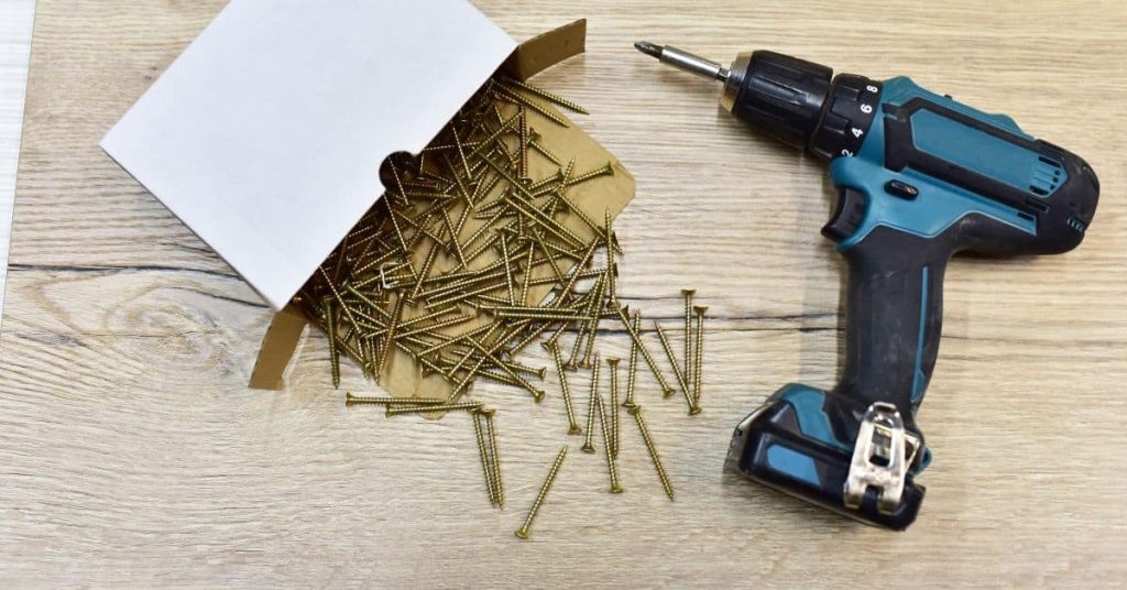 Cordless drill next to scattered box of screws on wood surface