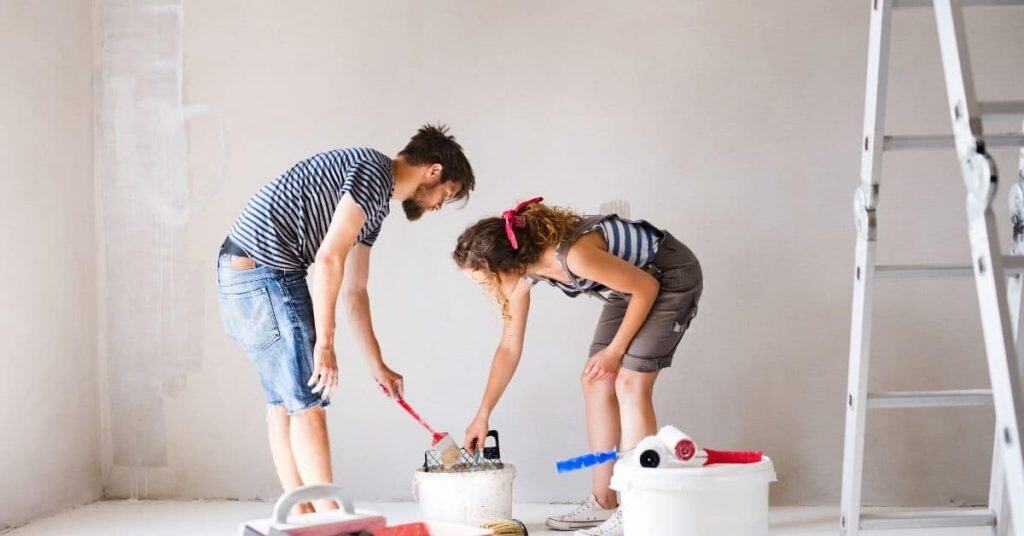 Couple preparing paint and tools in empty room