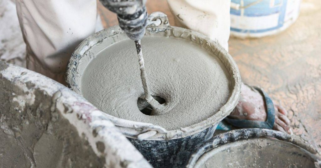 electric drill mixing cement in a bucket on dusty floor