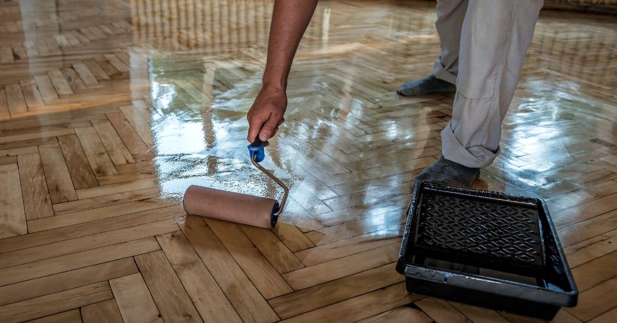 Person applying finish to hardwood floor with paint roller