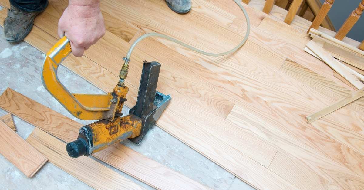 Hand holding nail gun installing hardwood flooring planks
