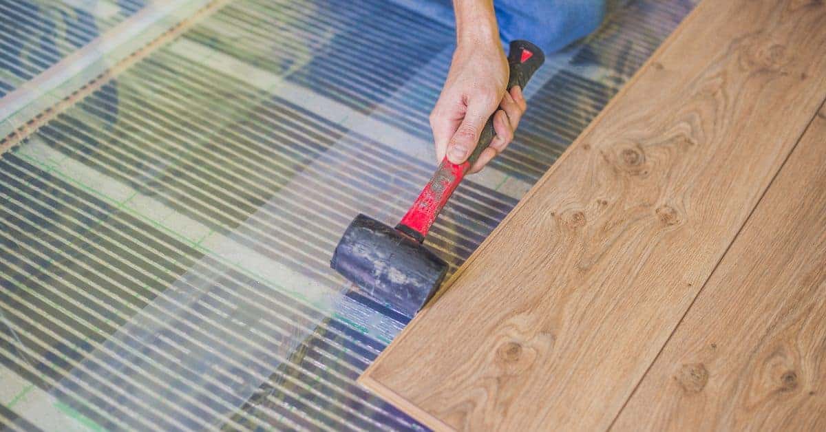 Hand with rubber mallet installing wood flooring over radiant heating