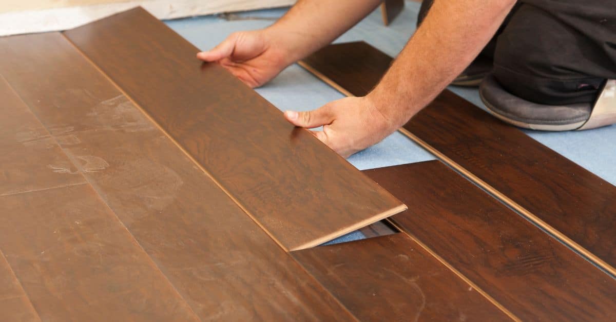 Hands installing dark brown laminate floor planks