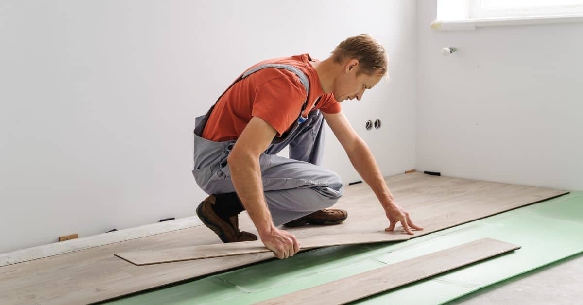 Man installing wood laminate flooring over green underlayment