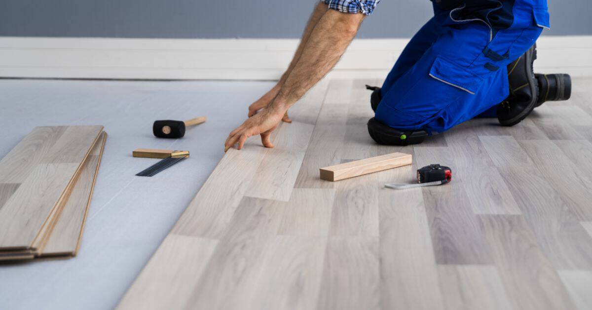 Person installing light gray laminate wood flooring on floor