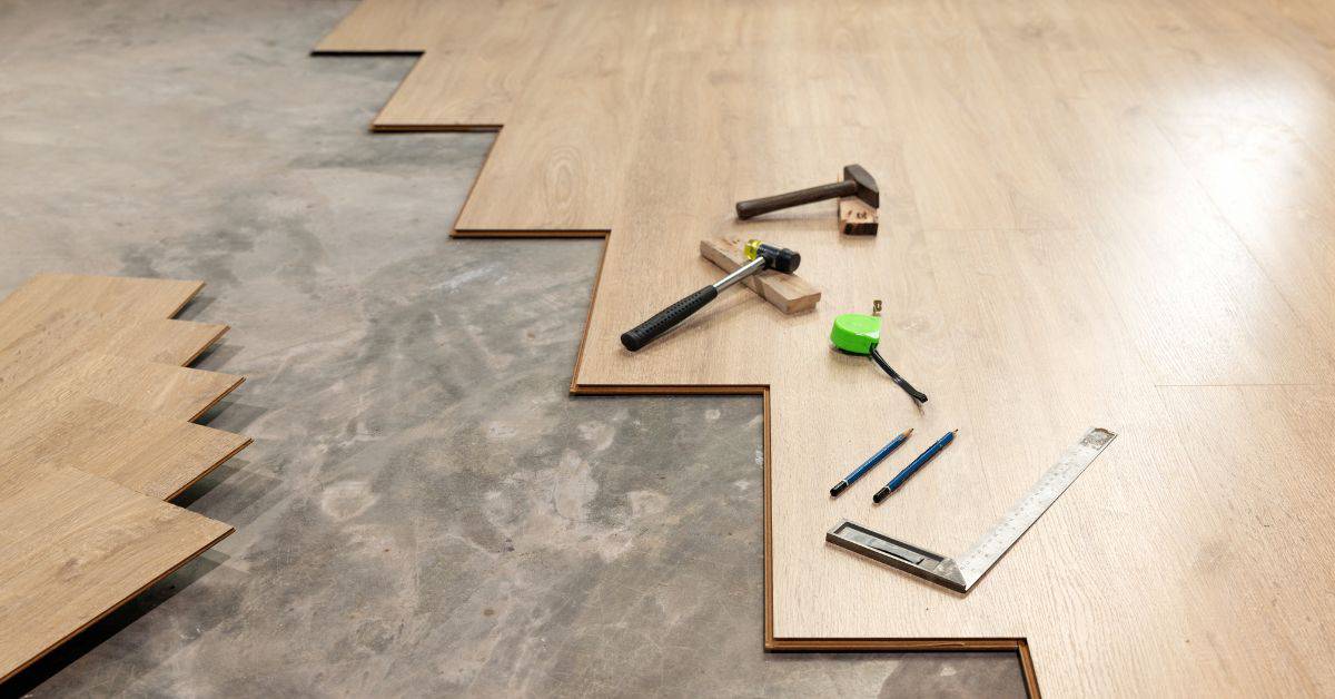 partially installed wooden laminate flooring with measuring tools and hammers