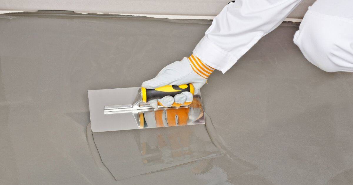 Hand wearing glove smoothing floor leveling compound with trowel