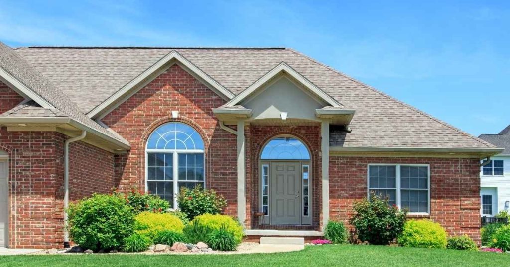 Front exterior of a brick house with windows and green shrubs