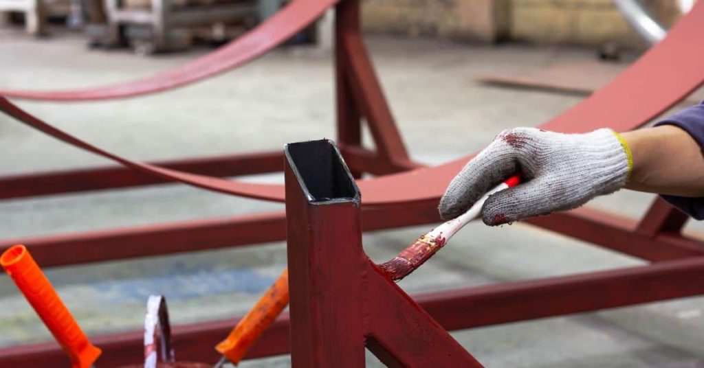 Gloved hand painting metal structure with red paintbrush