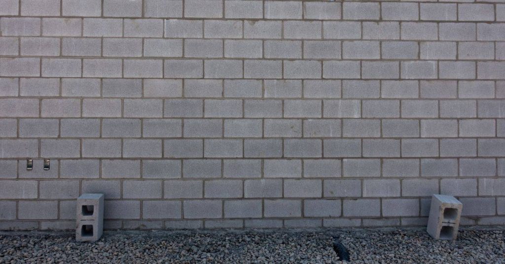 Gray concrete block wall with gravel base and two hollow concrete blocks
