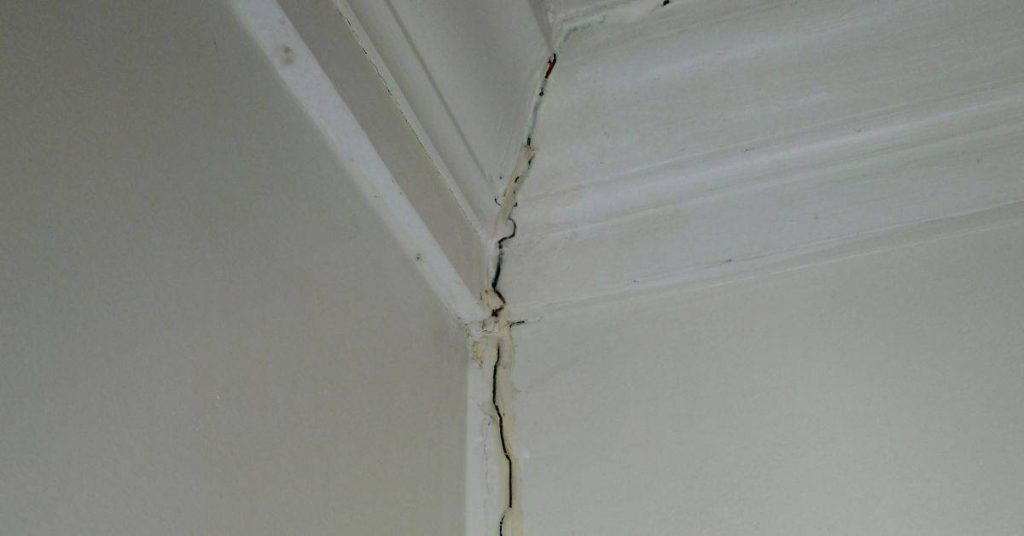 Hairline crack in plaster wall corner near ceiling trim