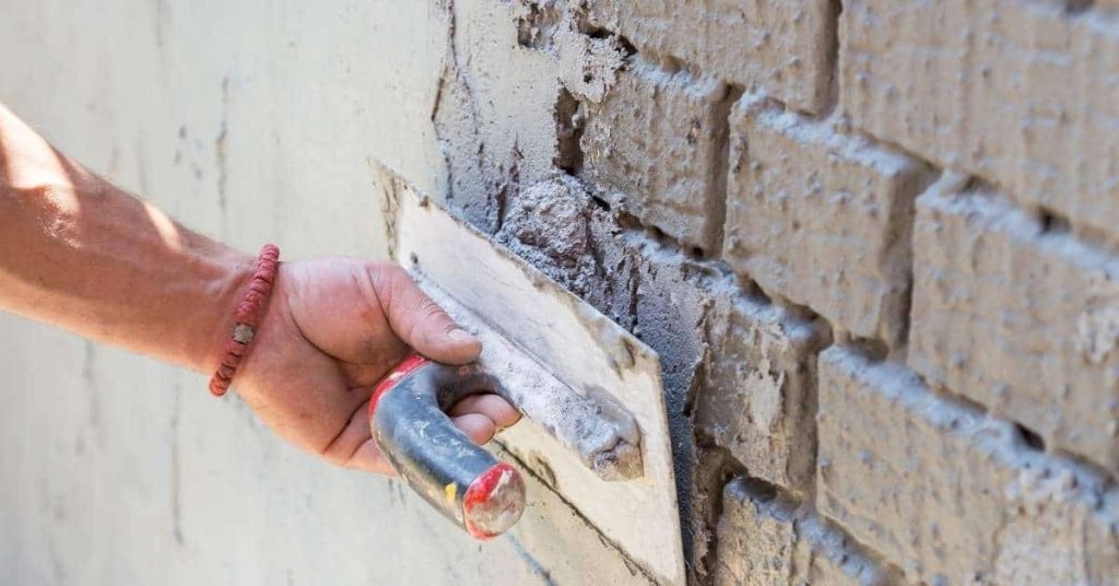 Hand applying plaster to brick wall with trowel