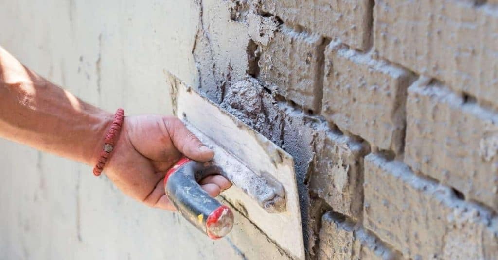 Hand applying plaster to brick wall with trowel