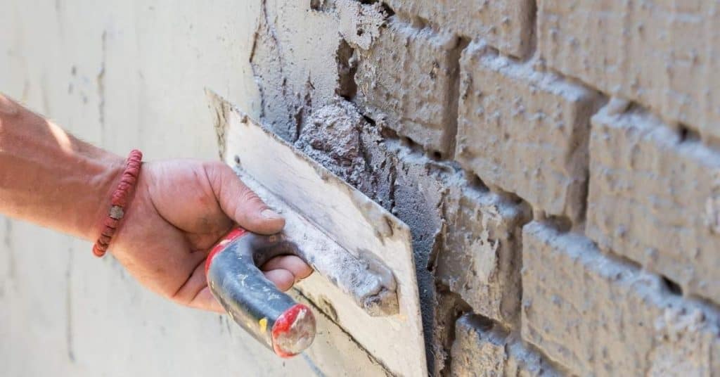 Hand applying plaster to rough brick wall with trowel
