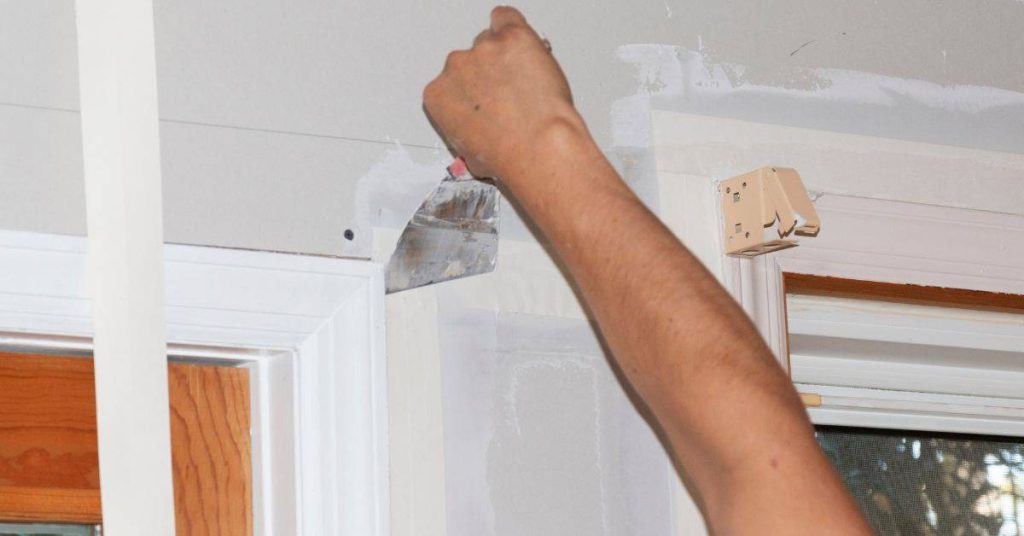 Hand applying spackle to drywall near a door frame