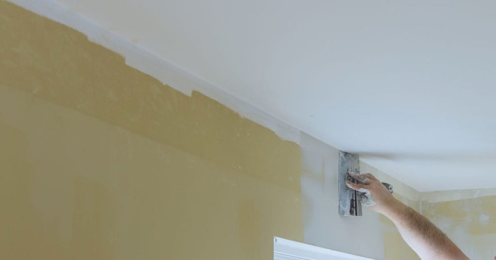 Hand applying spackle to wall near ceiling