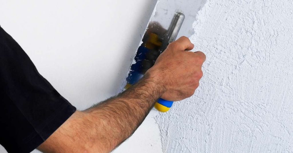 Hand applying textured plaster finish on wall with trowel