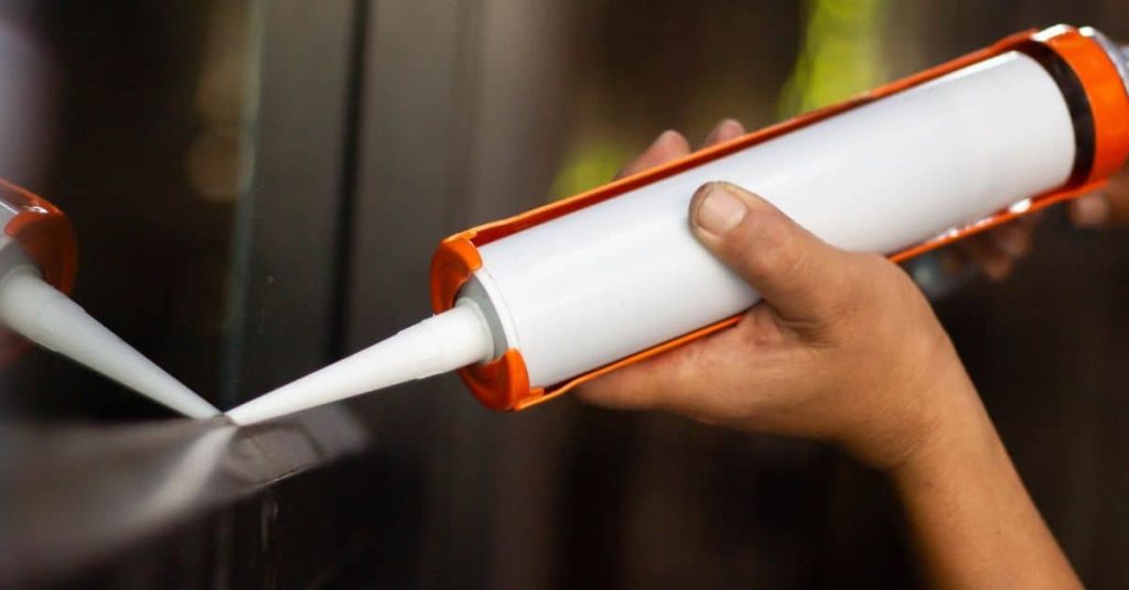 Hand applying white caulk from a caulking gun onto a surface