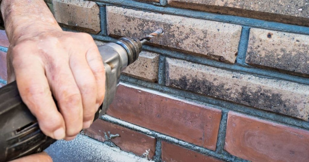 Hand holding drill bit drilling into brick mortar joint