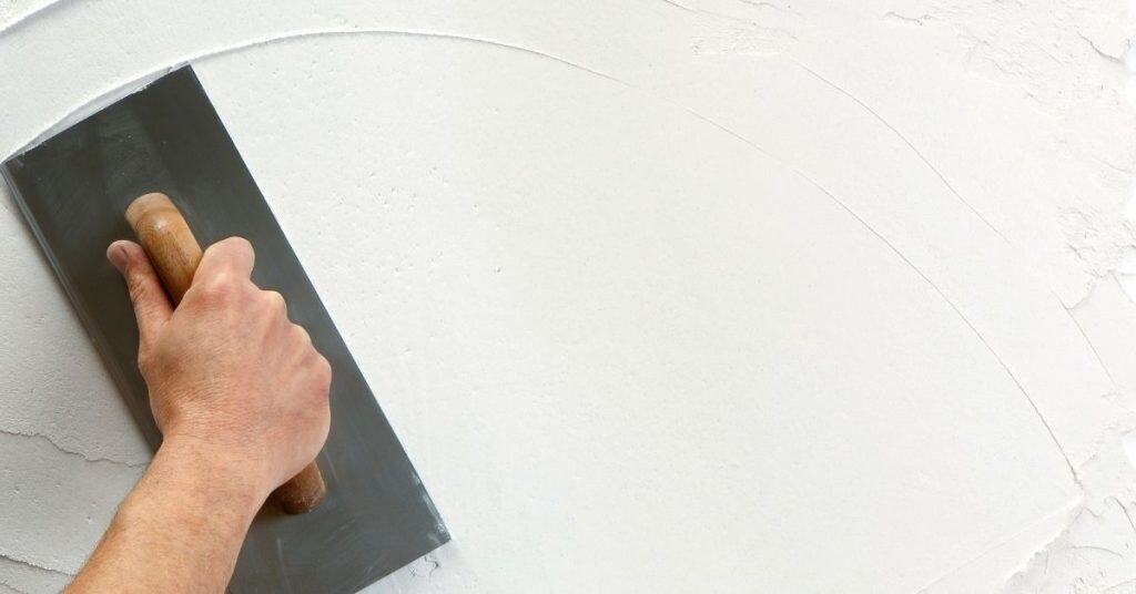 Hand holding trowel smoothing plaster on wall