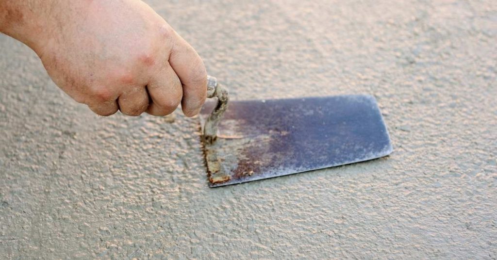 Hand holding trowel smoothing wet stucco surface