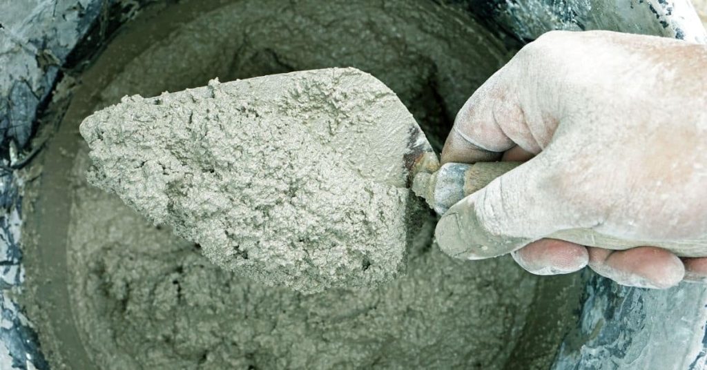 Hand holding trowel with wet concrete mixture