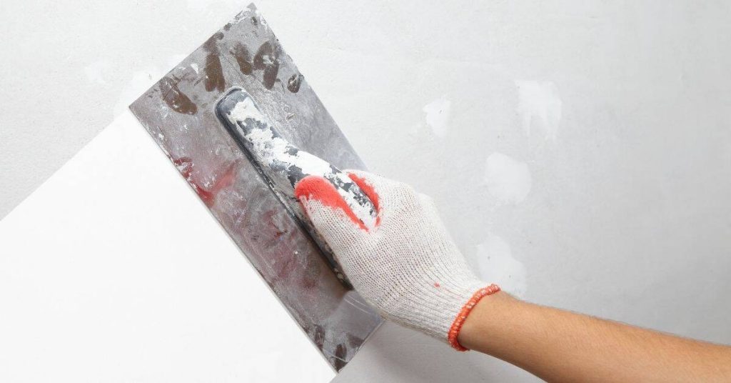 Hand in glove applying plaster with metal trowel on wall