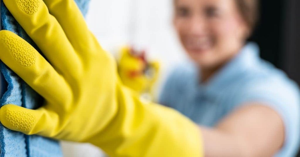 Hand in yellow glove cleaning blue surface with cloth