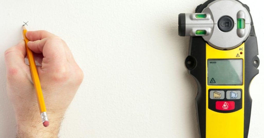 Hand marking wall with pencil next to electronic stud finder