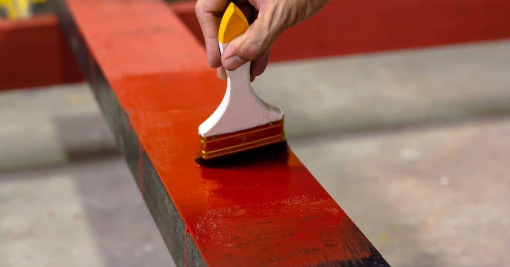 Hand painting metal beam with red primer brush