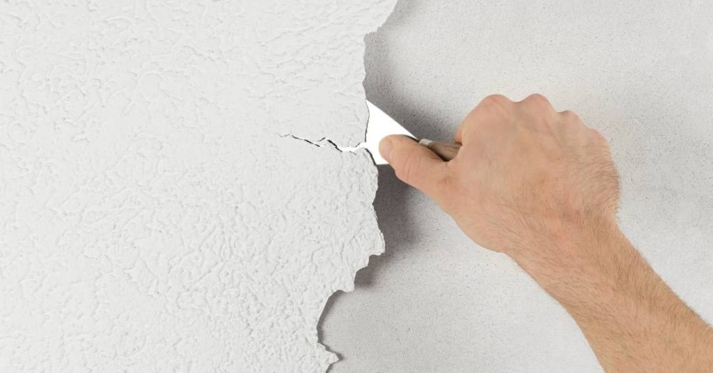 Hand scraping white stucco wall with metal scraper