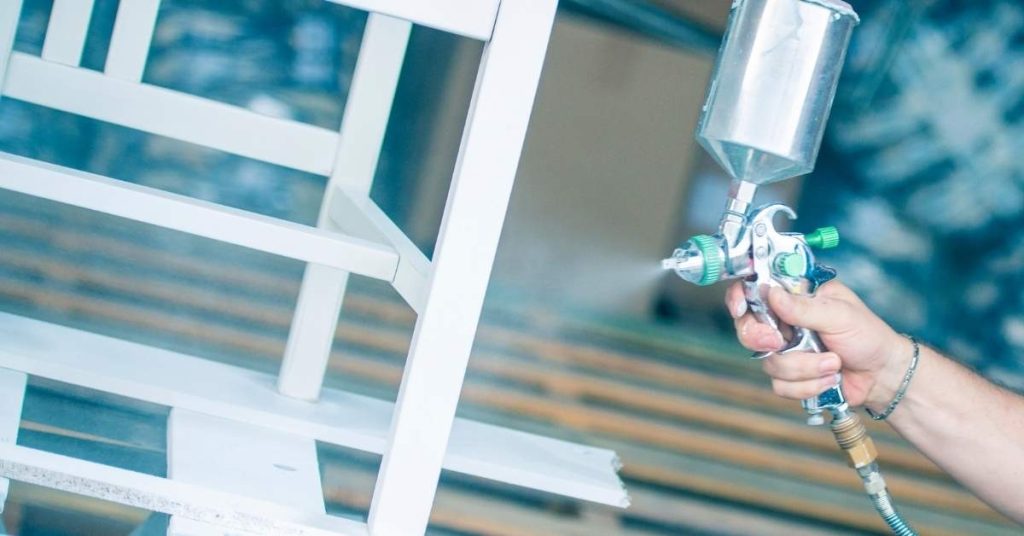 Hand spraying white lacquer on wooden furniture frame